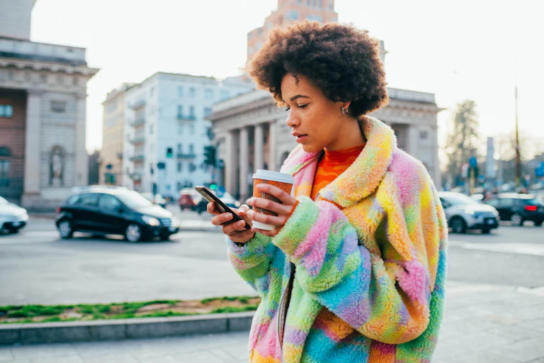 A young woman holding a reusable coffee cup while using a smartphone