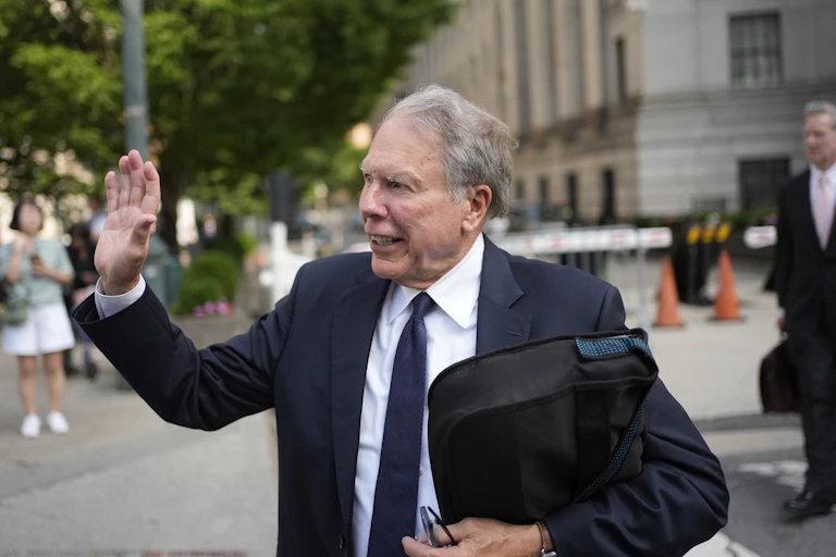 Man in navy suit and tie waves at someone.