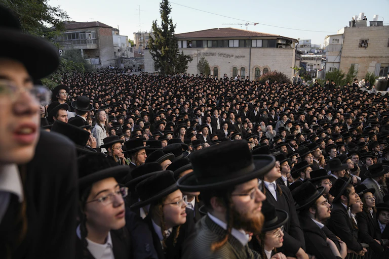 A crowd of hundreds of men outside, most of whom wear black jackets and black hats.