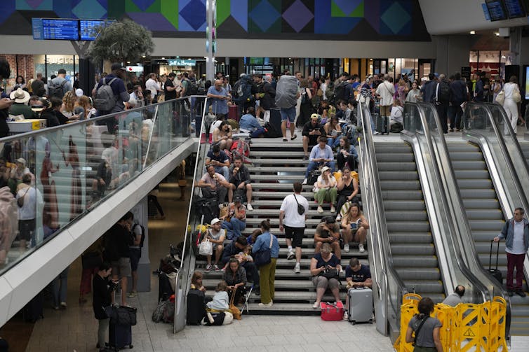 Travelers sit on steps at crowded Paris train station.