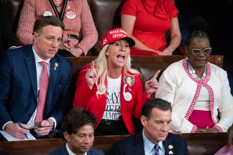 A woman in a red jacket and red baseball cap yells at someone.