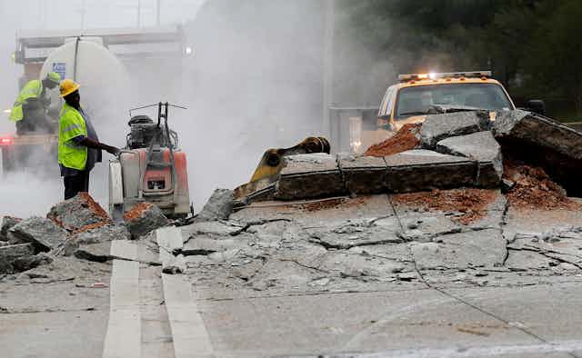 Workers with equipment examine a section of roadway that pushed up, with sections of road almost as high as one man's shoulder, in Atlanta in 2017.