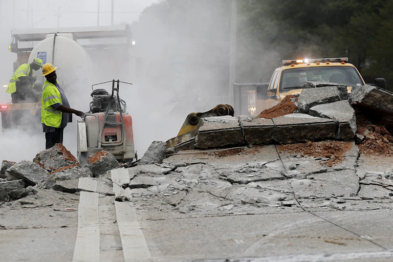 Workers with equipment examine a section of roadway that pushed up, with sections of road almost as high as one man's shoulder, in Atlanta in 2017.