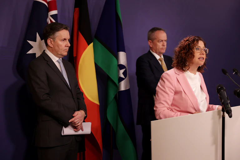one woman and two men stand in front of flags