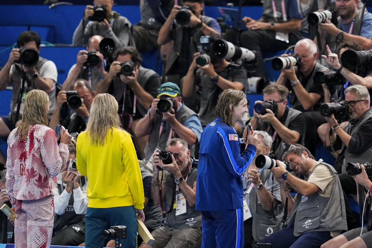 Three women stand in front of a wall of photographers