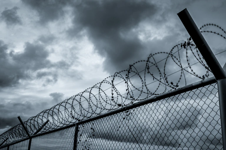 A prison security fence under a gloomy sky.