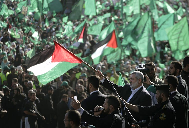 A man in a large crowd of people waves a big flag with black, white and green stripes and a red triangle