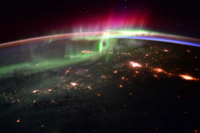 Curve of Earth at night with green and pink lights above it.