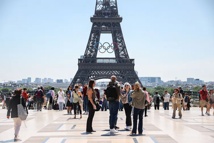 Tourists stand outside the Eiffel Tower, which bears the Olympic rings.