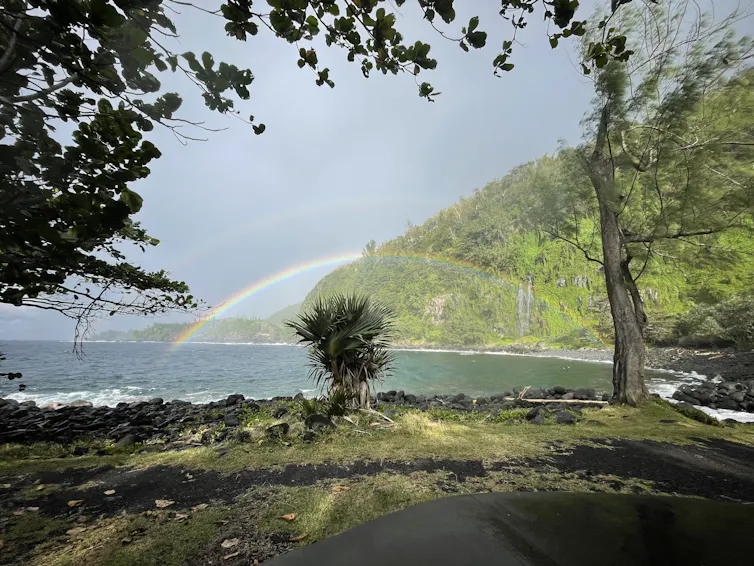 A rainbow arcs over the ocean alongside a verdant green hillside