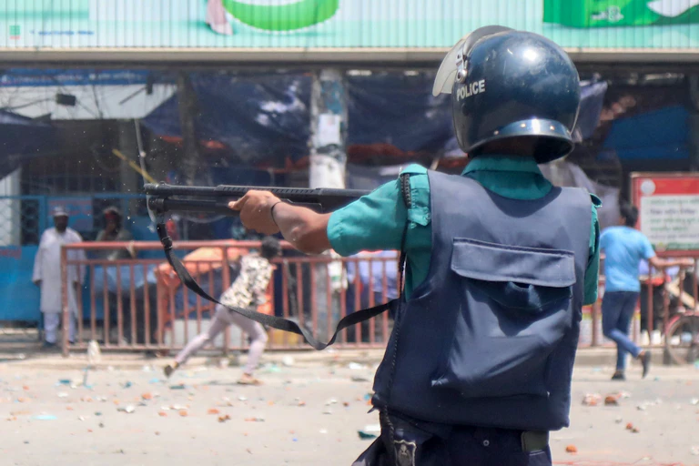 A Bangladeshi policeman firing a gun during a protest.