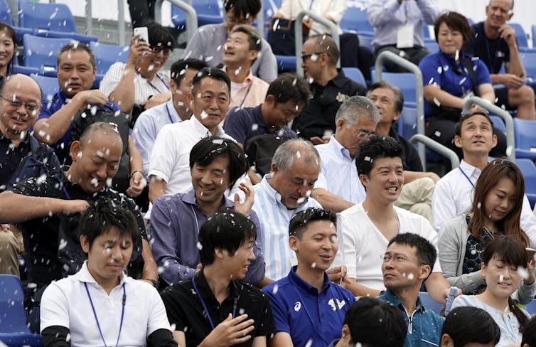 A stadium crowd are sprayed with artificial snow flakes.