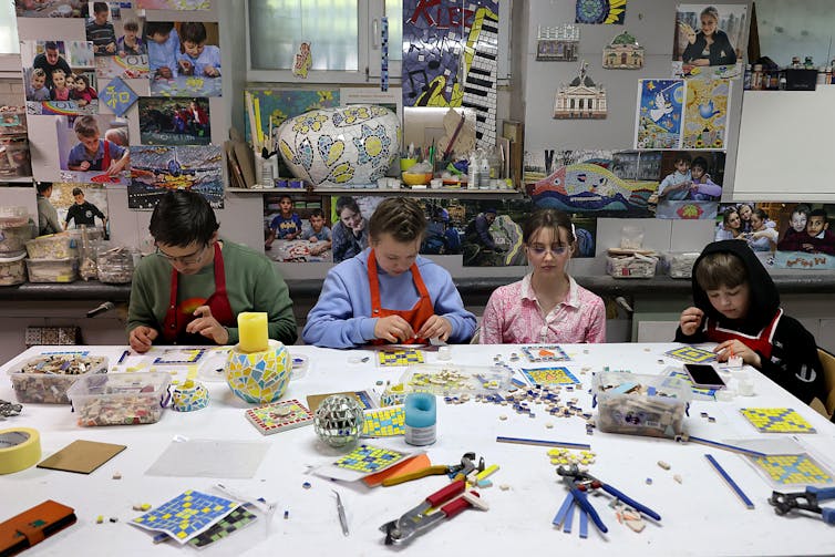 Four kids lost in concentration around an art table making mosaic tiles.
