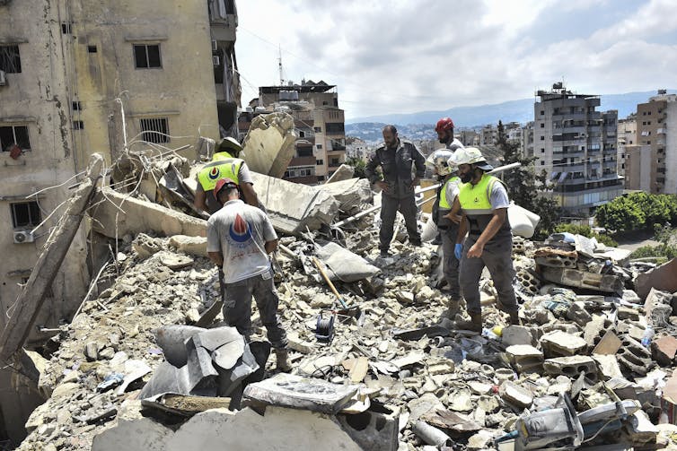A partially destroyed building is inspected by men in yellow jackets.