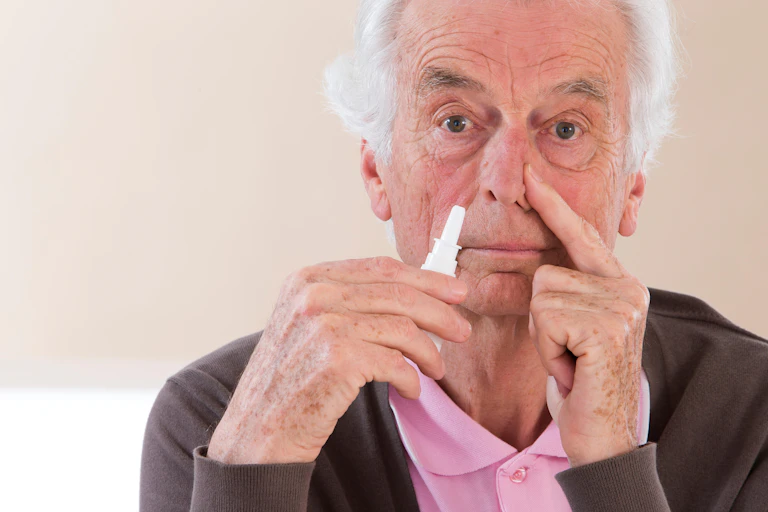 Homem idoso segurando um frasco de spray nasal próximo ao nariz.