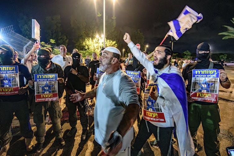 A man draped in a blue and right flag leads chants during a protest.