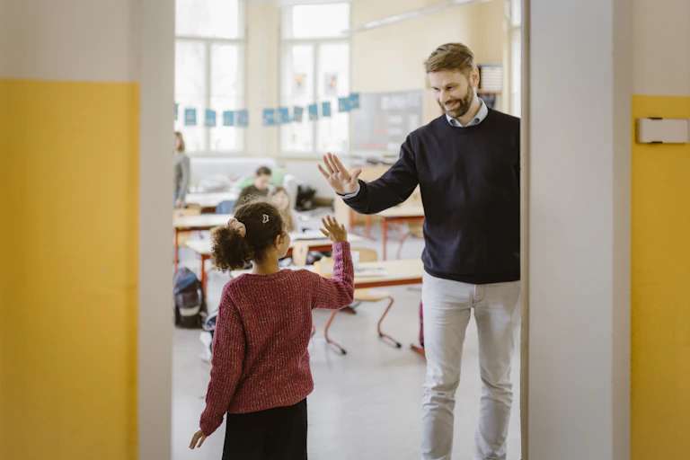 A male teacher gives a high-five to a young female student.