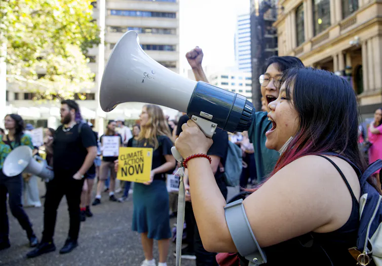 A young woman speaks into a megaphone in front of other young people holding signs