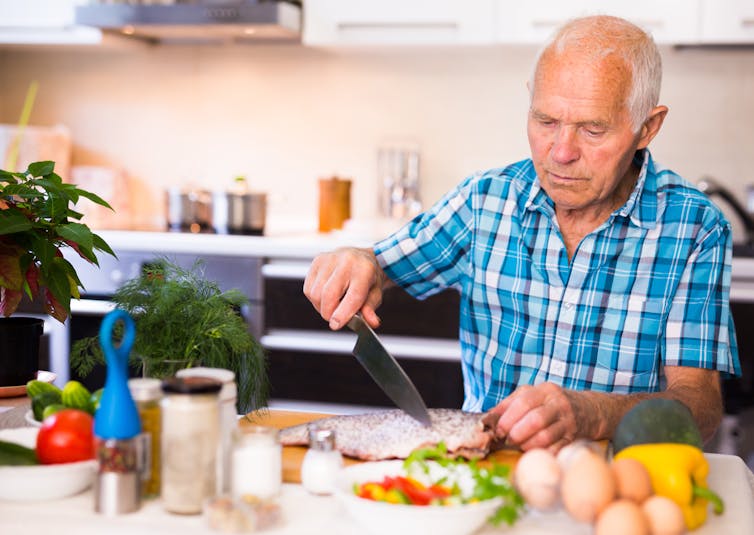 An older man in the kitchen prepares a fish for cooking.