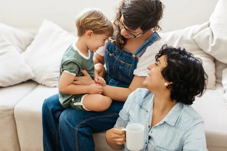 Woman sitting on sofa with toddler on lap, female partner sitting on ground