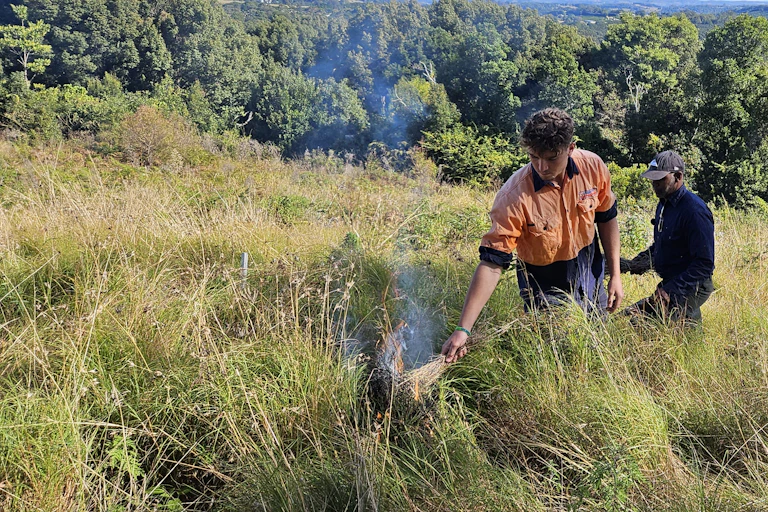 man lights grass fire as another man watches