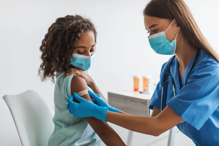 A nurse puts a bandaid on a girl's upper arm.