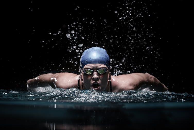 Simmer in blue cap breaking through the water against dark background