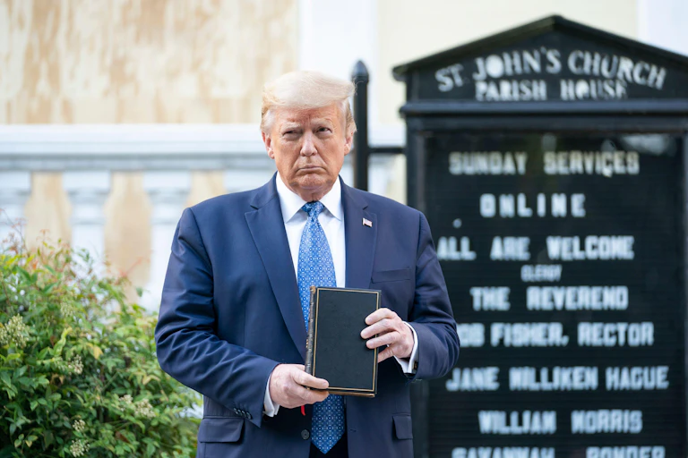 Donald Trump stands in front of a church signboard holding a bible.
