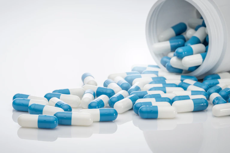 Blue and white pills spilling out of a white pill bottle.