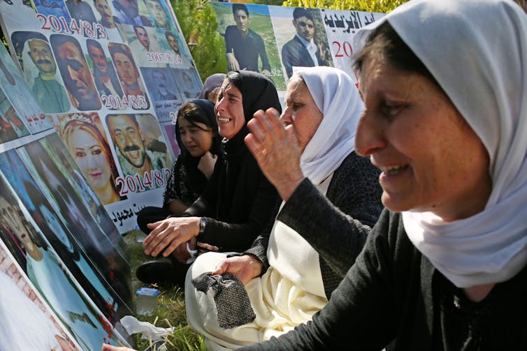 Yazidi women cry in front of pictures of the victims of the Yazidi genocide.