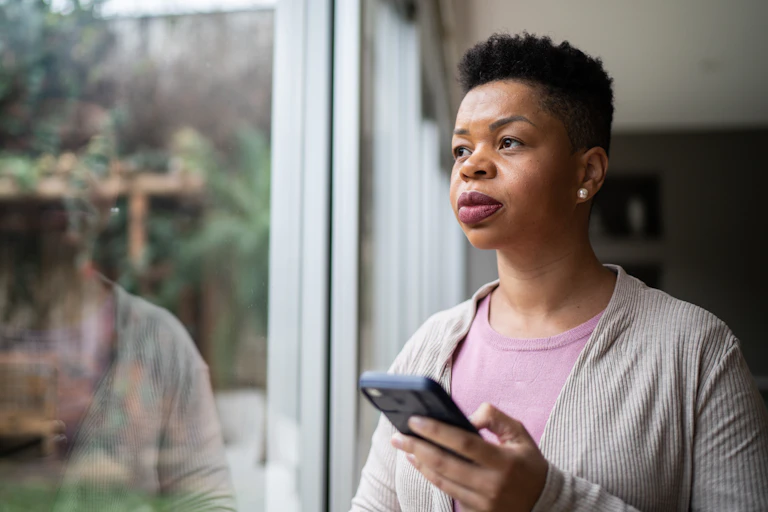 woman holding cellphone looks pensively into distance
