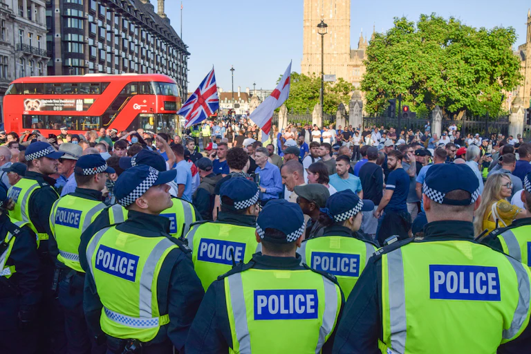 A crowd of police seen from behind, with a group of protesters in front of them, holding union jack and england flags