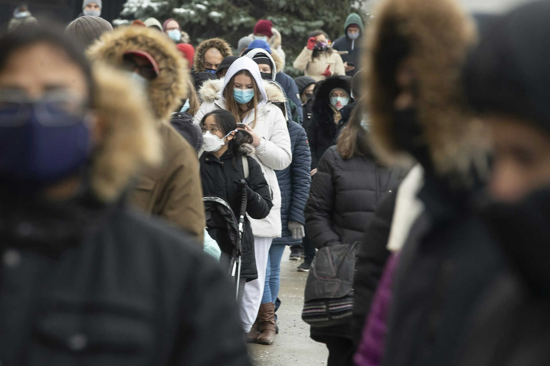A crowd of people in winter clothing and face masks