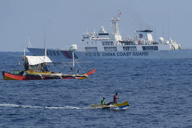 Un navire des garde-côtes chinois surveille des pêcheurs philippins à bord d'un bateau en bois