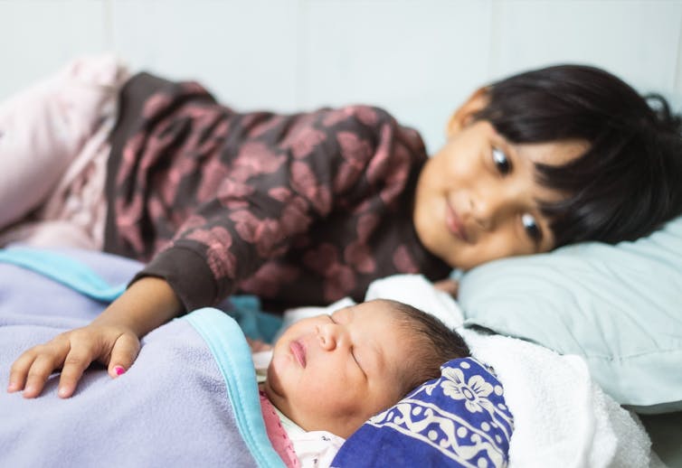 A child has a hand resting on an infant's belly.