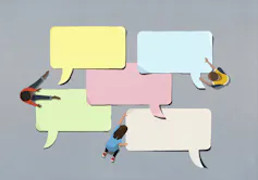 Seen from above, three kids arrange big paper speech bubbles on the ground.
