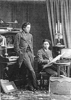 Anton leans against a piano; Nikolay draws.