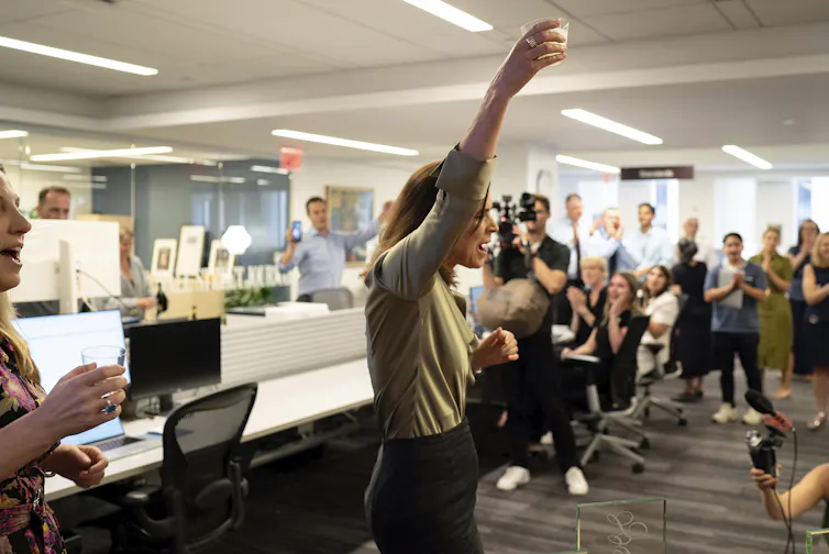 A woman in a newsroom holds a drink high above her head
