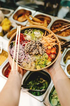 Hands holding a bowl full of vegetables, with chopsticks.