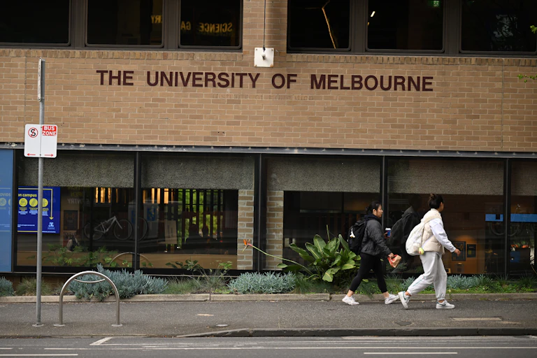 Two people walk past a building that says 'The University of Melbourne'.