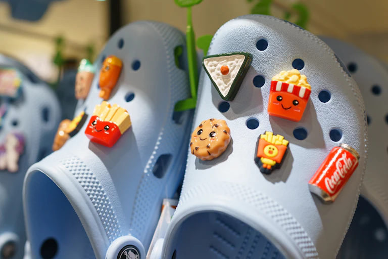 Des crocs avec des pins représentant des frites un cookie et un coca cola plantés dans les petits trous de la chaussure