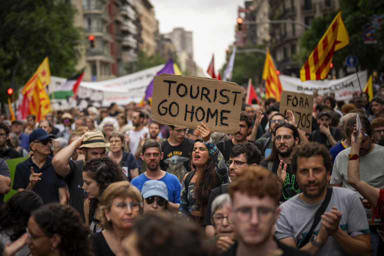 Personas en una protesta, una lleva una pancarta que dice: turista vete a casa