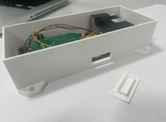 A white metal rectangular box about 16cm in length with wires and a green motherboard inside