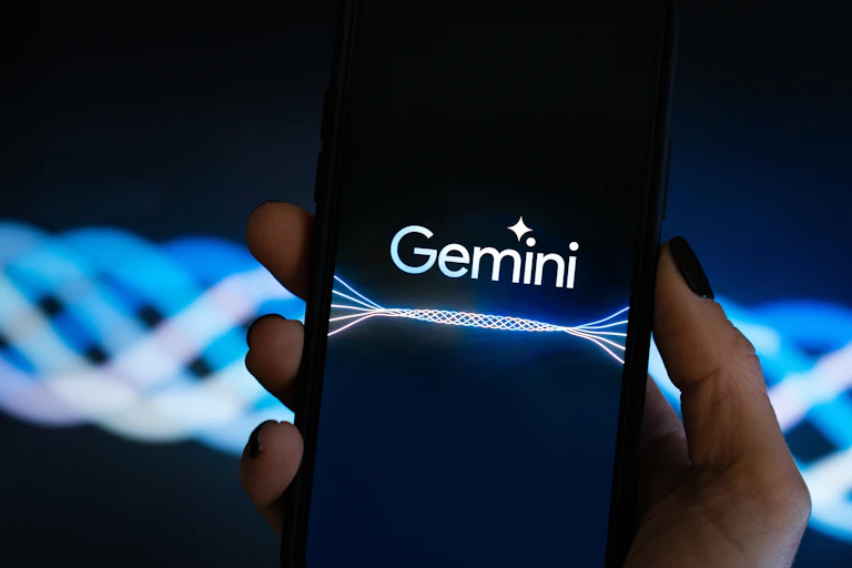A hand holding up a smartphone with the Gemini logo on the screen