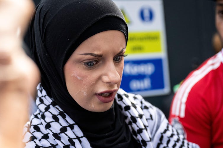 A woman wearing a headscarf with spit on her face.