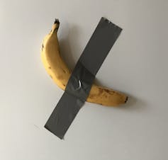 A banana stuck to a wall with grey tape.
