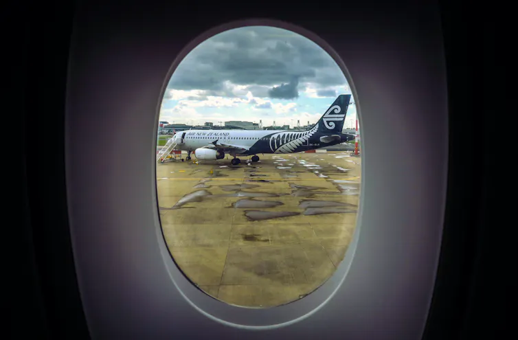 An Air New Zealand plane can be seen through the window of another plane as it sits on the tarmac at Auckland International Airpor