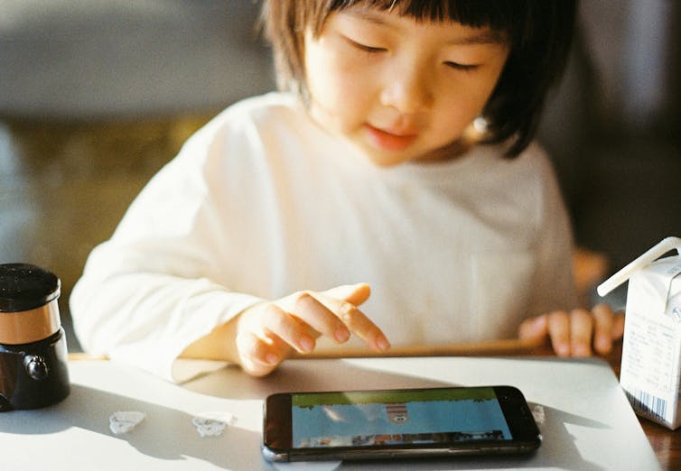 A young child looks at a carton on a mobile phone.