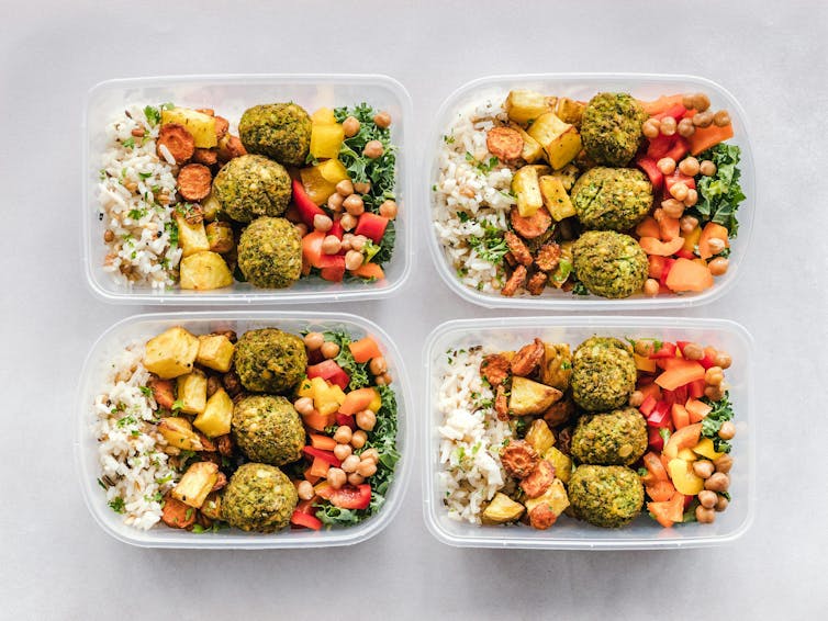 Four containers of food including rice, falafels, legumes and vegetables.