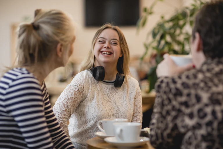 woman with down syndrome sits in cafe talking to two other people over coffee